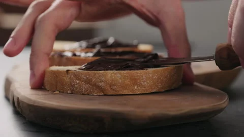 Slow motion man spreading chocolate spread on ciabatta slice on olive board Video stock 292397503