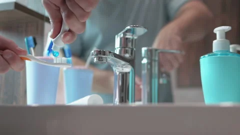 Slow motion A man squeezes toothpaste onto a blue toothbrush under a water tap Stock Footage 213581957