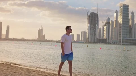 Slow motion man with sunglasses walking on the beach with Dubai Marina skyline Stock Footage 280701678
