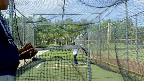 Slow motion of man throwing baseball to kid inside batting cages Stock Footage 85653566