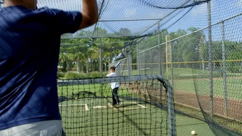 Slow motion of man throwing baseball to kid who misses inside batting cages Stock Footage 85653595