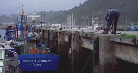 Slow motion of man tying rope of docked boat to pier in harbour on cloudy day Video stock 158646127