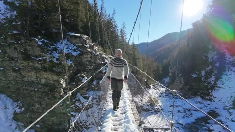 Slow motion man Walking Across Suspension Bridge Over River in Snowy Alps Stock-Footage 326180461