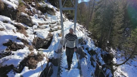 Slow motion man Walking Across Suspension Bridge Over River in Snowy Alps Stock-Footage 326180485