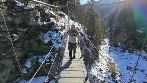 Slow motion man Walking Across Suspension Bridge Over River in Snowy Alps Video stock 326180487