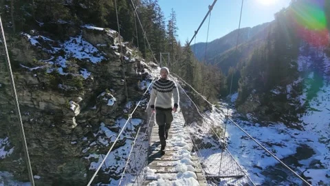 Slow motion man Walking Across Suspension Bridge Over River in Snowy Alps Video stock 326180492