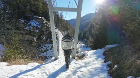 Slow motion man Walking Across Suspension Bridge Over River in Snowy Alps Video stock 326180514