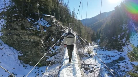 Slow motion man Walking Across Suspension Bridge Over River in Snowy Alps Video stock 326180520
