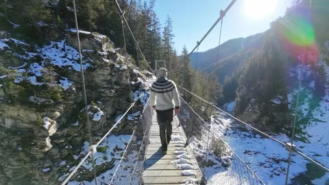 Slow motion man Walking Across Suspension Bridge Over River in Snowy Alps Video stock 326180535