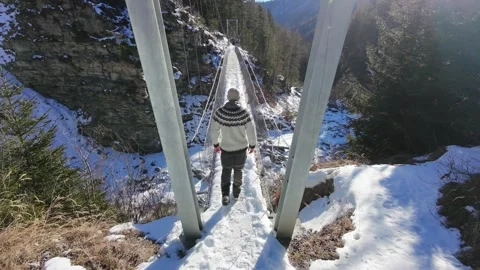 Slow motion man Walking Across Suspension Bridge Over River in Snowy Alps Video stock 326180545