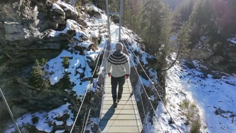 Slow motion man Walking Across Suspension Bridge Over River in Snowy Alps Stock-Footage 326180562