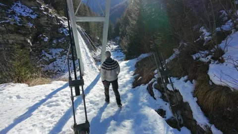 Slow motion man Walking Across Suspension Bridge Over River in Snowy Alps Stock Footage 326180565