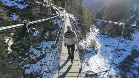 Slow motion man Walking Across Suspension Bridge Over River in Snowy Alps Stock Footage 326180572