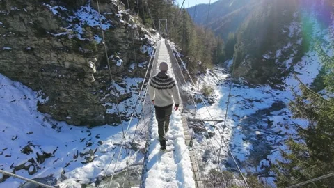 Slow motion man Walking Across Suspension Bridge Over River in Snowy Alps Video stock 326180608