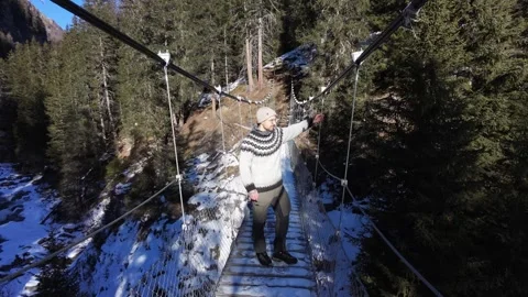 Slow motion man Walking Across Suspension Bridge Over River in Snowy Alps Stock Footage 326180626