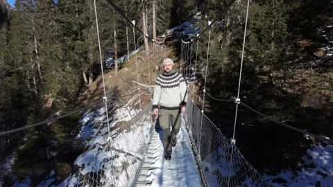 Slow motion man Walking Across Suspension Bridge Over River in Snowy Alps Video stock 326180631
