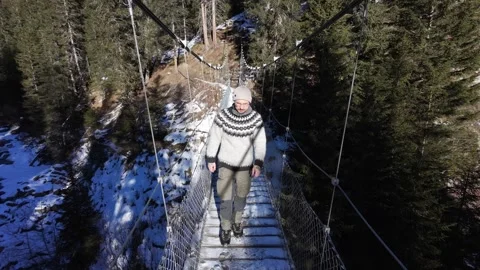 Slow motion man Walking Across Suspension Bridge Over River in Snowy Alps Stock-Footage 326180639