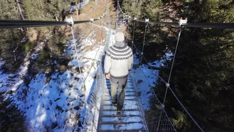 Slow motion man Walking Across Suspension Bridge Over River in Snowy Alps Video stock 326180643