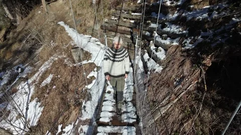 Slow motion man Walking Across Suspension Bridge Over River in Snowy Alps Video stock 326180651