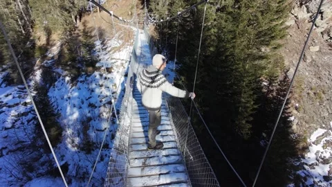 Slow motion man Walking Across Suspension Bridge Over River in Snowy Alps Video stock 326180659