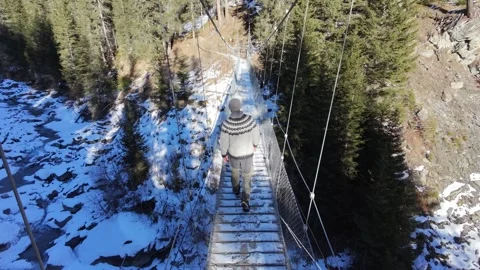 Slow motion man Walking Across Suspension Bridge Over River in Snowy Alps Stock-Footage 326180660