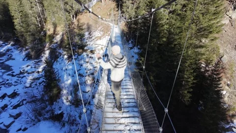 Slow motion man Walking Across Suspension Bridge Over River in Snowy Alps Video stock 326180673