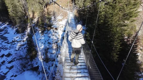 Slow motion man Walking Across Suspension Bridge Over River in Snowy Alps Video stock 326180683