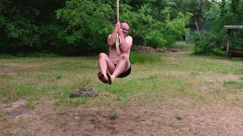 Slow motion of man wearing just briefs holding to rope and swing back and forth Stock Footage 244985396