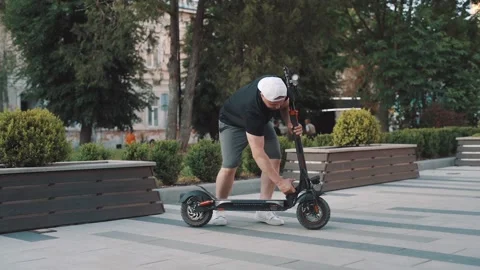 Slow motion of man in white cap riding electric scooter in city Stock-Footage 229258155
