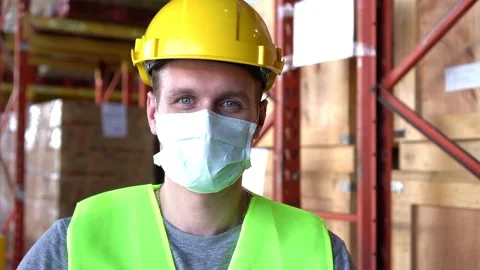 Slow motion man worker wear mask and open mask sit near shelf in warehouse 動画素材 153384863