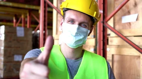 Slow motion man worker wear mask and thumbs up sit near shelf in warehouse 動画素材 153384868