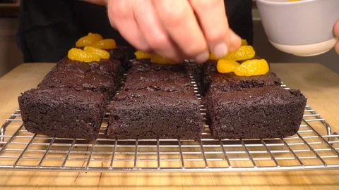 Slow motion – Man’s hand placing mandarin pieces on chocolate brownies. Video stock 104039822