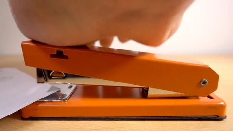 Slow motion – Man’s hand using an orange office stapler. Stock Footage 104949024