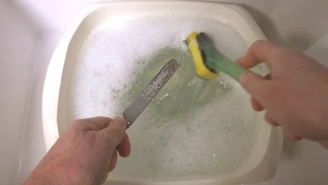 Slow motion: Man’s hands cleaning knife with a scourer in a bowl of soapy water. Stock-Footage 98928474