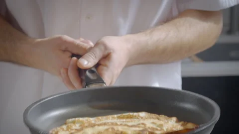 Slow-motion of a man's hands flipping pancakes, crepes in the air from a pan. Stock Footage 274463147