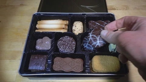 Slow motion – Man’s hands opening lid and choosing from box of luxury biscuits. Stock Footage 100751423