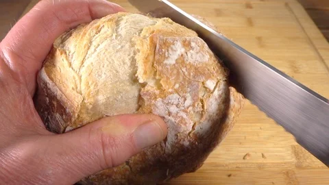 Slow motion - Man’s hands slicing a piece of bread from a fresh loaf. Video stock 104559626