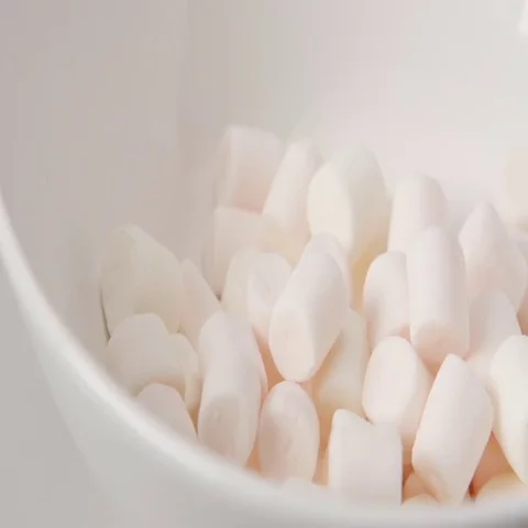 SLOW MOTION: Marshmallows fall on white dish (close up) Stock Footage 69477374