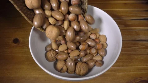 Slow motion – Mixed unshelled nuts being poured into a bowl, with nutcrackers. Video stock 121874387