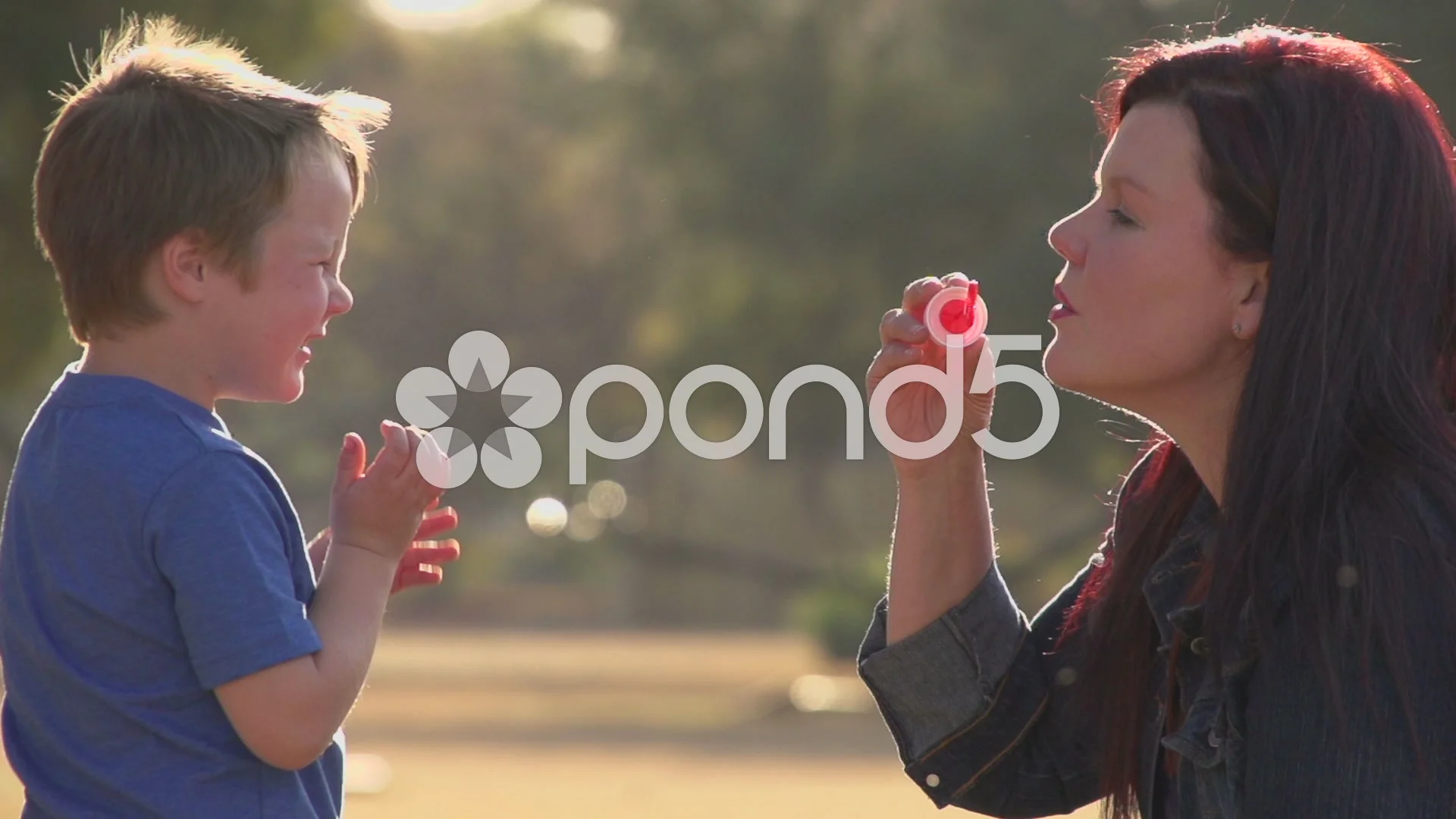 Slow motion of mother blowing bubbles towards child, child laughing happily