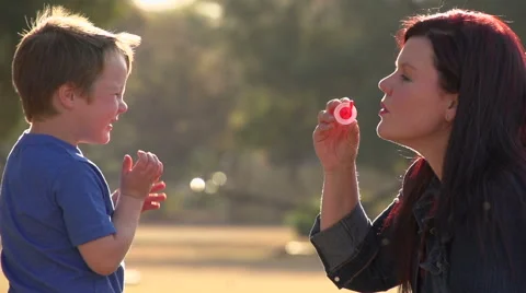 Slow motion of mother blowing bubbles towards child, child laughing happily Stock Footage 46376445