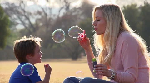 Slow motion of mother blowing bubbles towards child, child laughing happily Stock Footage 46376457