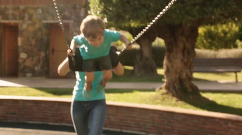 Slow motion of mother pushing son on swing in park. Video stock 43669200