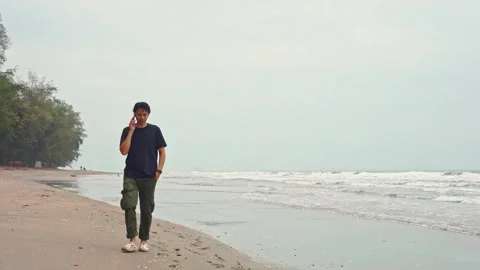 Slow motion moving of wave with asian man walk and use phone on sand beach Stock Footage 254541359