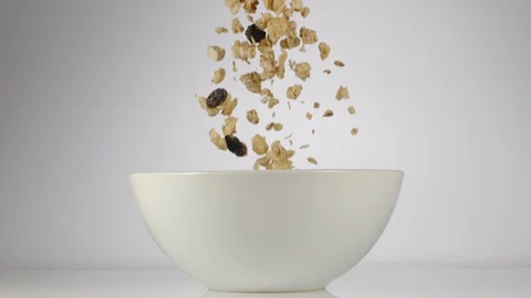 SLOW MOTION: Muesli falling in a white dish on a table Stockbeeldmateriaal 108959596