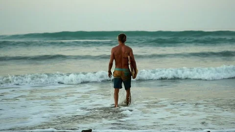 Slow motion: Muscular surfer guy walks beach to surf, holding surfboard  Stock Footage 108565190