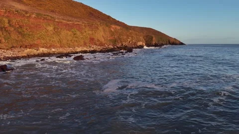 Slow Motion Ocean Waves Along Sunlit Coastal Hillside in 4K Stockbeeldmateriaal 332944391