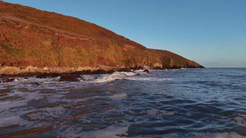 Slow Motion Ocean Waves Along Sunlit Coastal Hillside in 4K Video stock 332944421