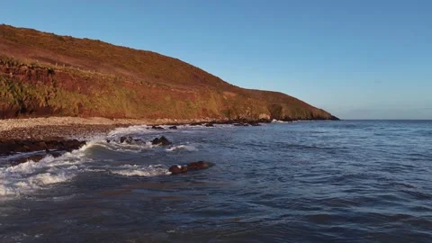Slow Motion Ocean Waves Along Sunlit Coastal Hillside in 4K Stock Footage 332944433