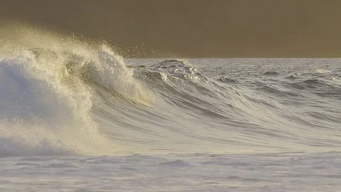 SLOW MOTION: Offshore wind creating large crashing waves at orange lit sunset. Stock Footage 84497692